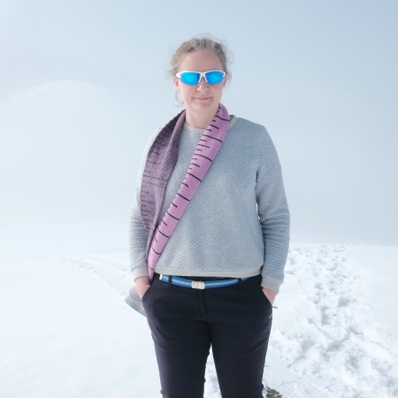 Woman wearing grey sweatshirt, a pink scarf and blue wrap-around sunglasses standing in a snowy landscape